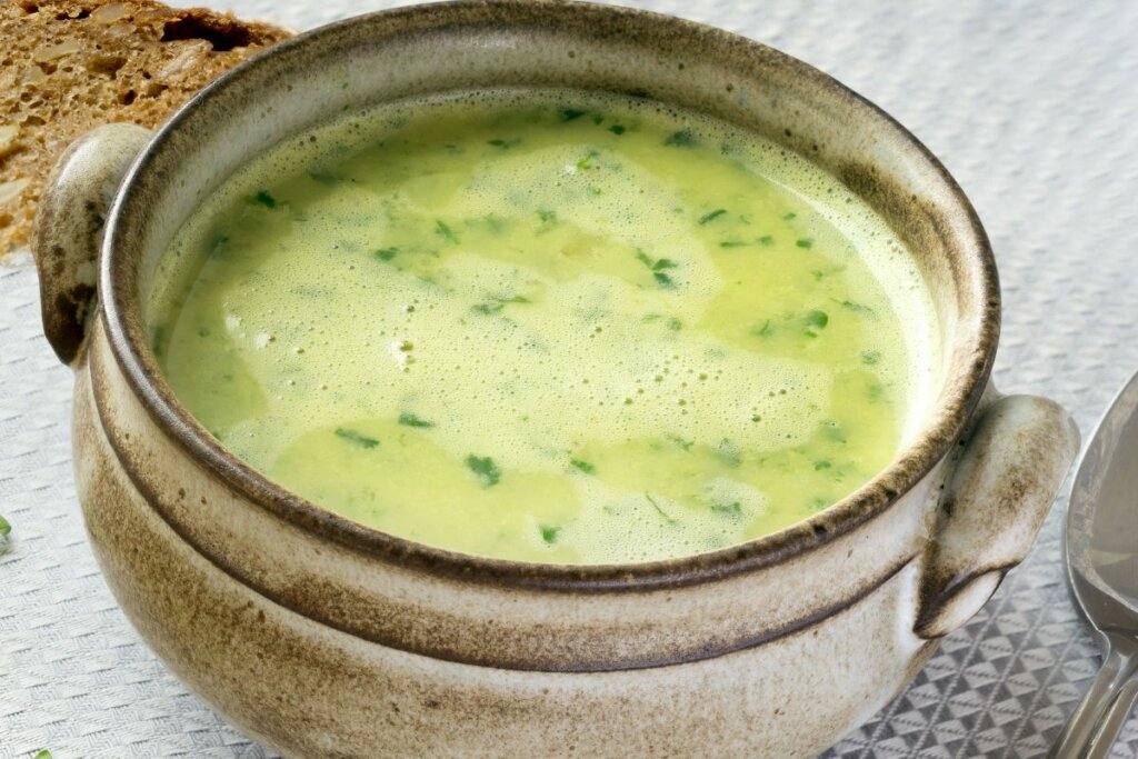 Panela com sopa verde em cima de uma mesa branca
