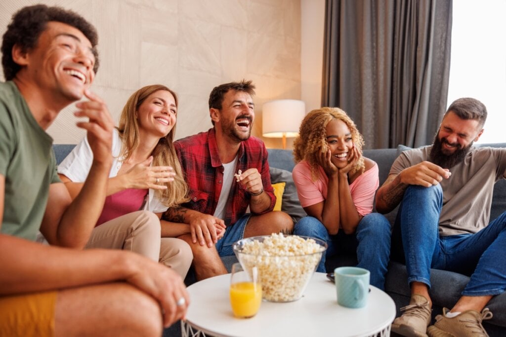 Amigos sentados em sofá assistindo a filme de comédia em TV e comendo pipoca