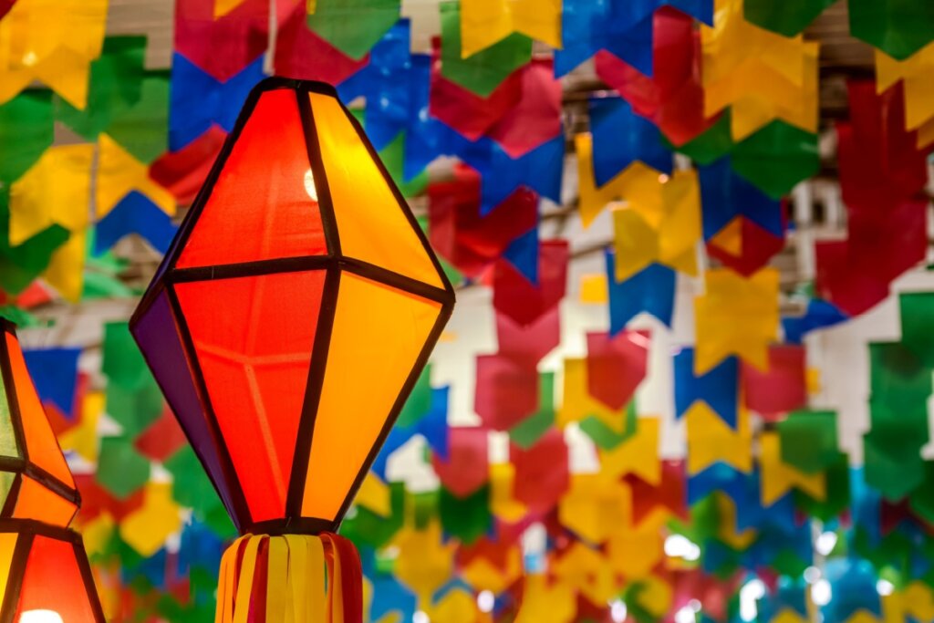 Imagem de decoração de festa junina, há um balão colorido pendurado no teto junto a diversas bandeirinhas coloridas