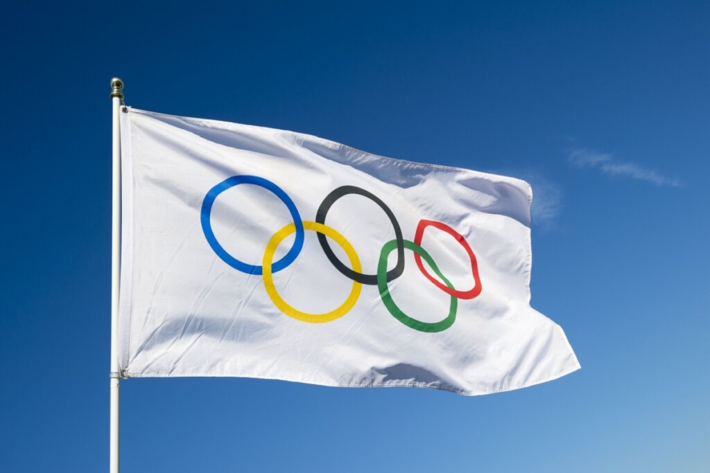 Bandeira branca com os cinco arcos das Olimpíadas com céu azul ao fundo