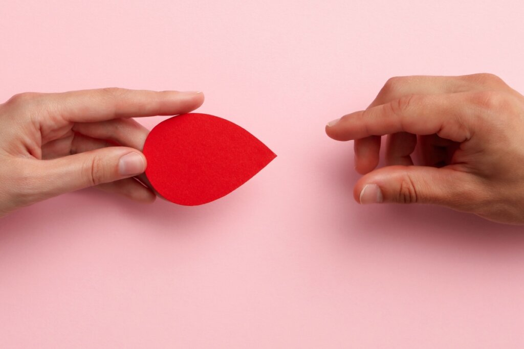 duas mãos trocando a imagem de uma gota de sangue em um fundo rosa