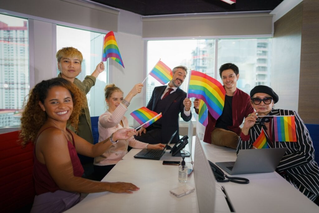 Equipe em sala corporativa sorrindo com bandeira LGBTQIAPN+