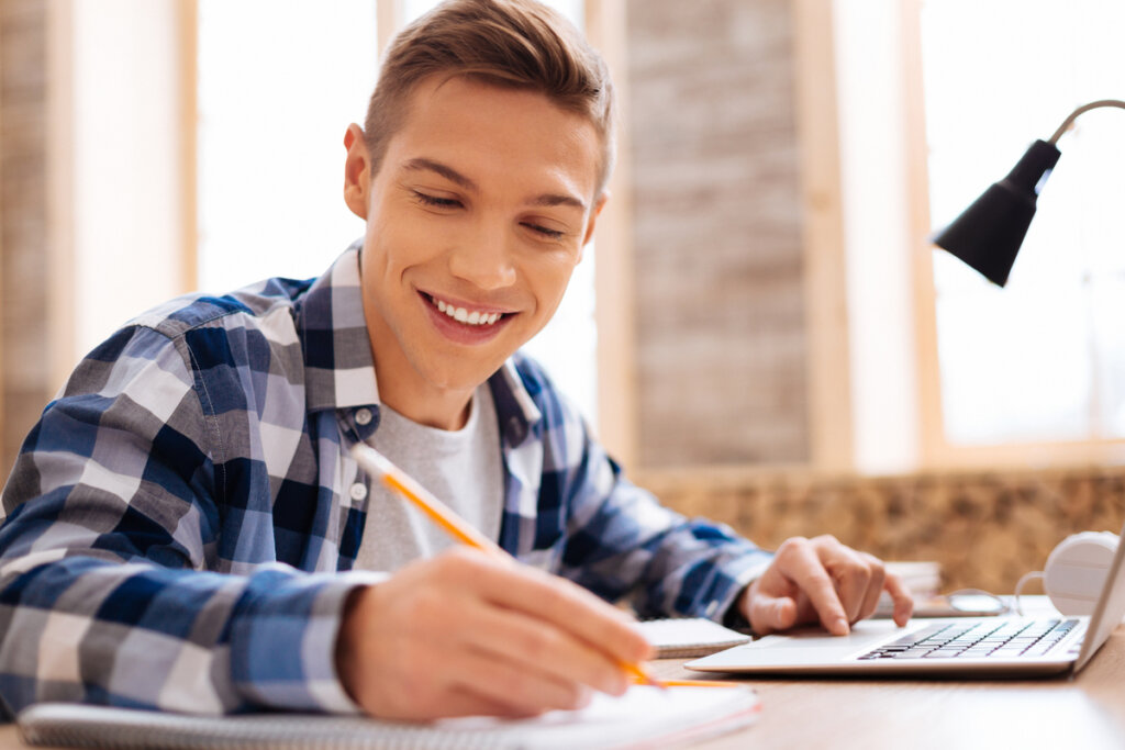 estudante sorrindo enquanto escreve e usa computador