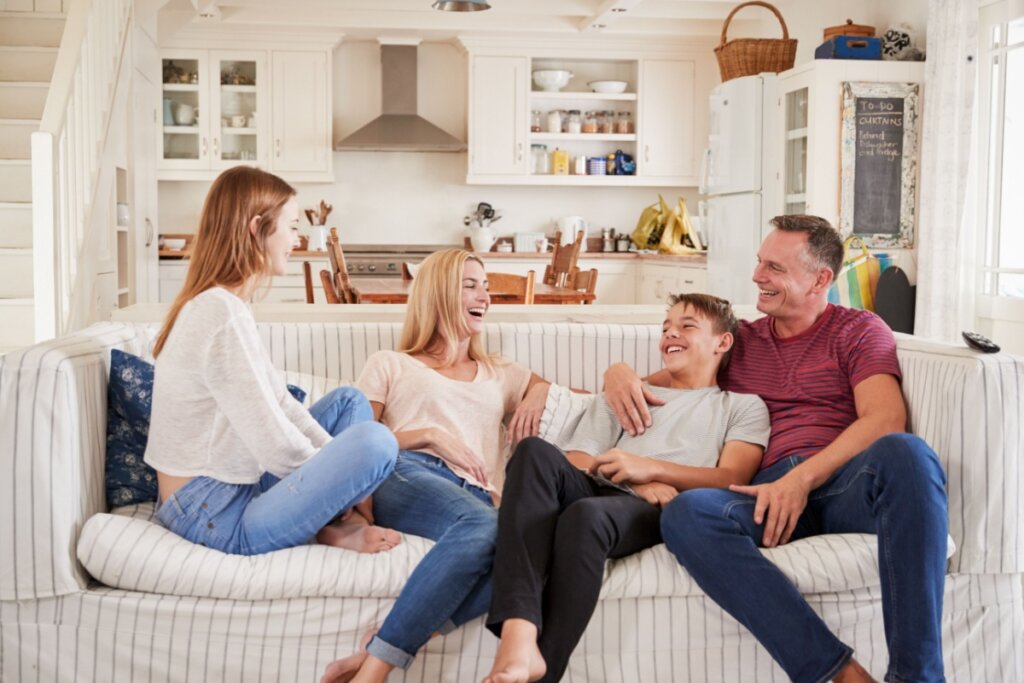 Família sentada no sofá conversando e rindo, com pai, mãe e dois filhos, uma menina e um menino adolescentes