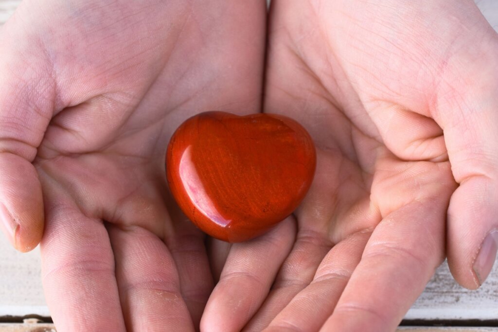 Um cristal jaspe vermelho no formato semelhante de um coração sendo segurado por duas mãos. 
