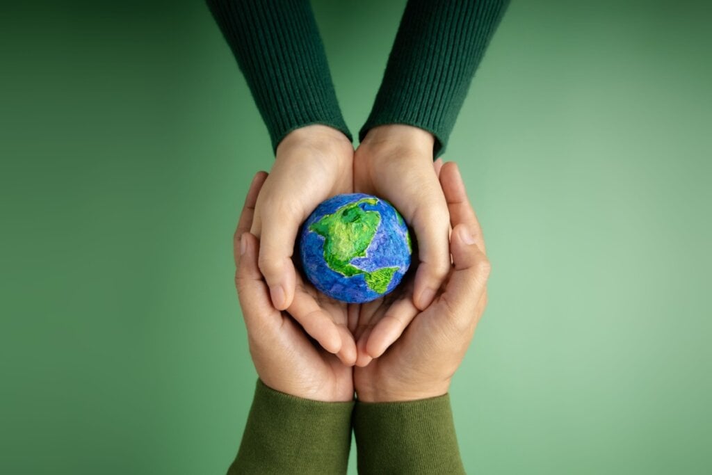Duas pessoas segurando na mão uma representação do planeta Terra, em fundo verde escuro.