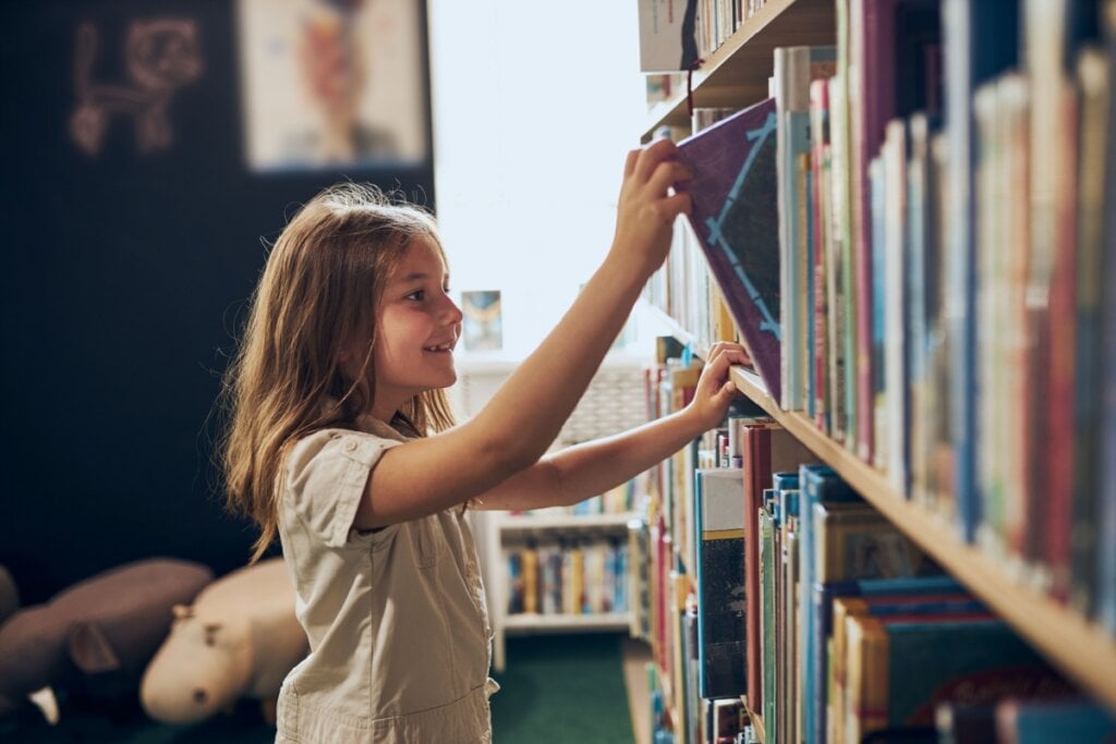 Menina tirando livro de prateleira em biblioteca