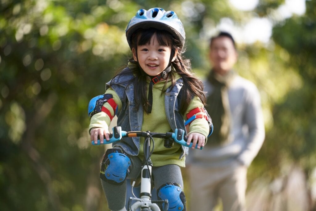 menina andando de bicicleta com equipamentos de proteção: capacete, joelheira e cotoveleira 