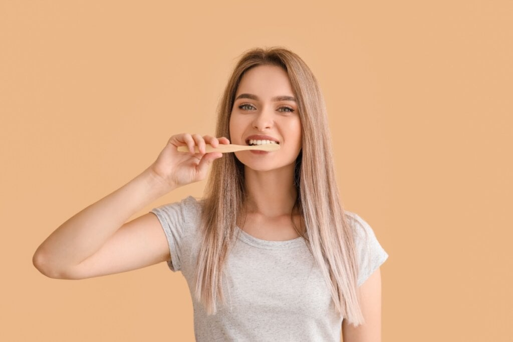 Mulher loira de camiseta cinza escovando os dentes com escova de madeira