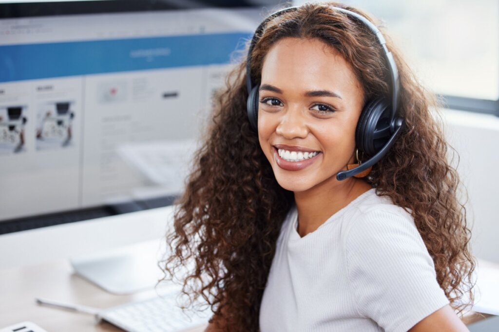 Mulher usando fone de ouvido e sorrindo com computador atrás