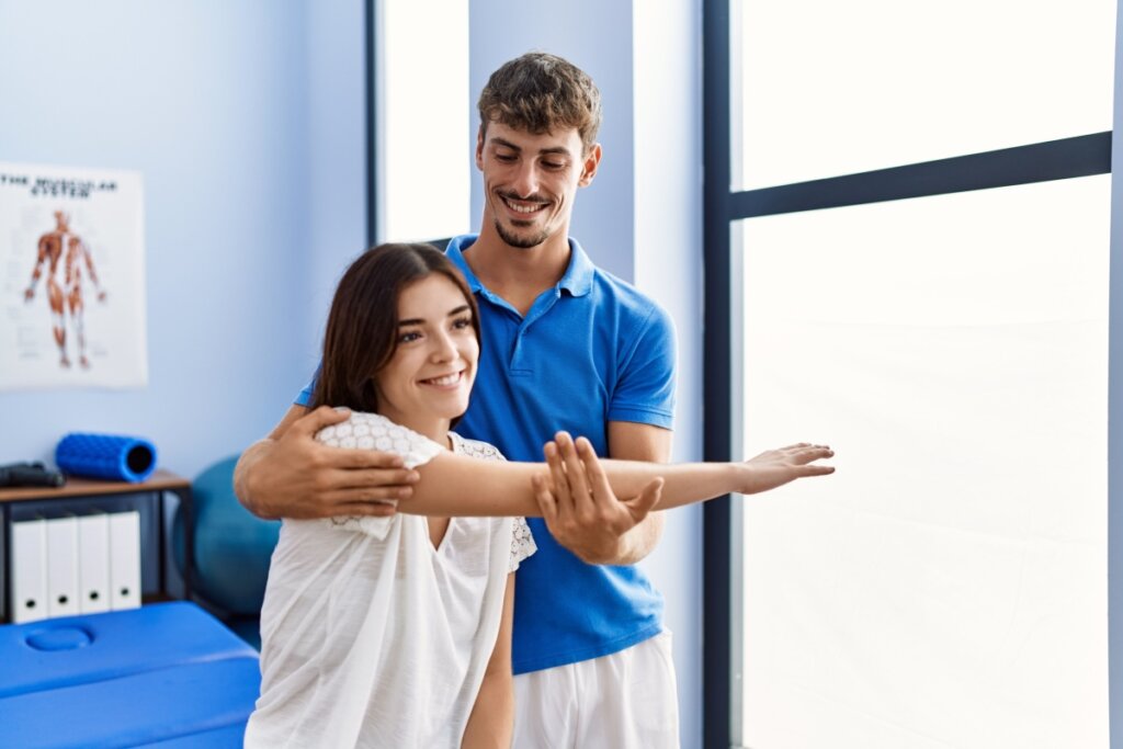Homem de azul atrás de mulher puxando o braço dela para o lado em quiropraxia