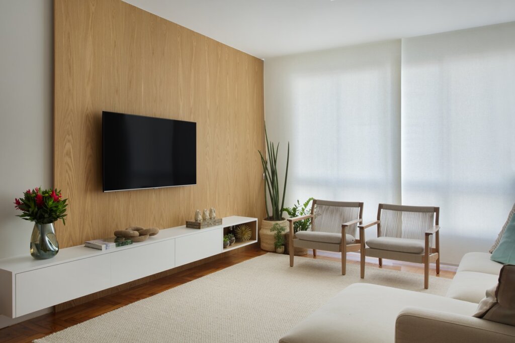 Imagem de sala de estar com tons claros e terrosos em poltronas, rack e sofá 