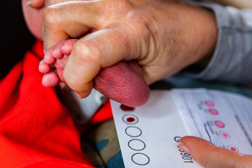Imagem de uma enfermeira fazendo a coleta de sangue do calcanhar de um recém-nascido para realização do teste do pezinho 
