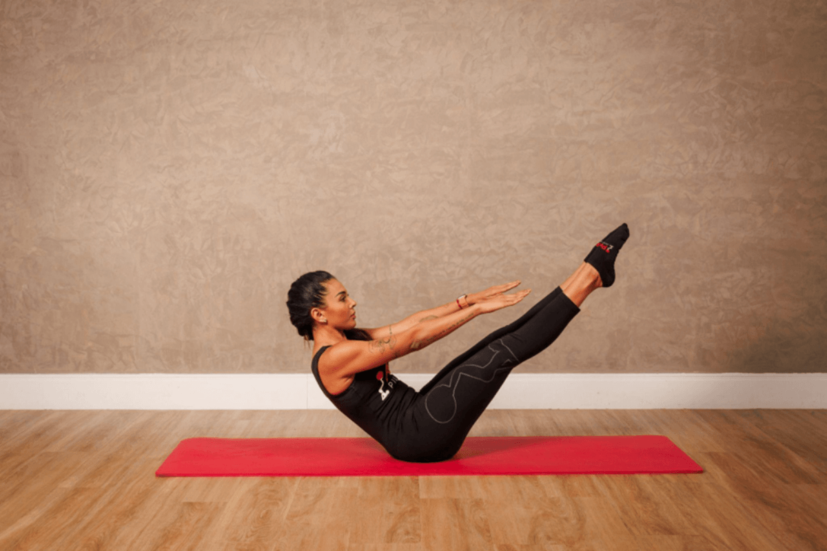 Mulher fazendo exercícios de pilates no chão em tapete vermelho usando roupas de academia preta