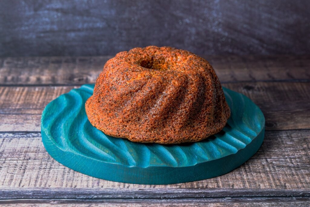 Bolo de coco redondo em cima de uma travessa verde em uma mesa de madeira