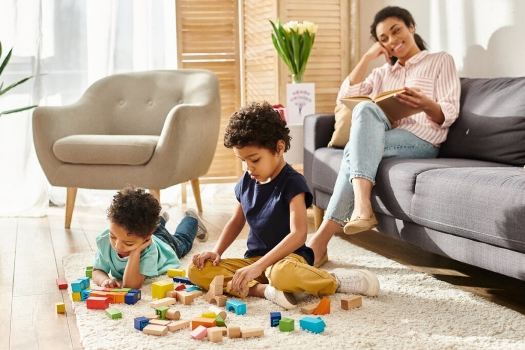 Crianças brincando em um tapete enquanto a mãe lê em um sofá