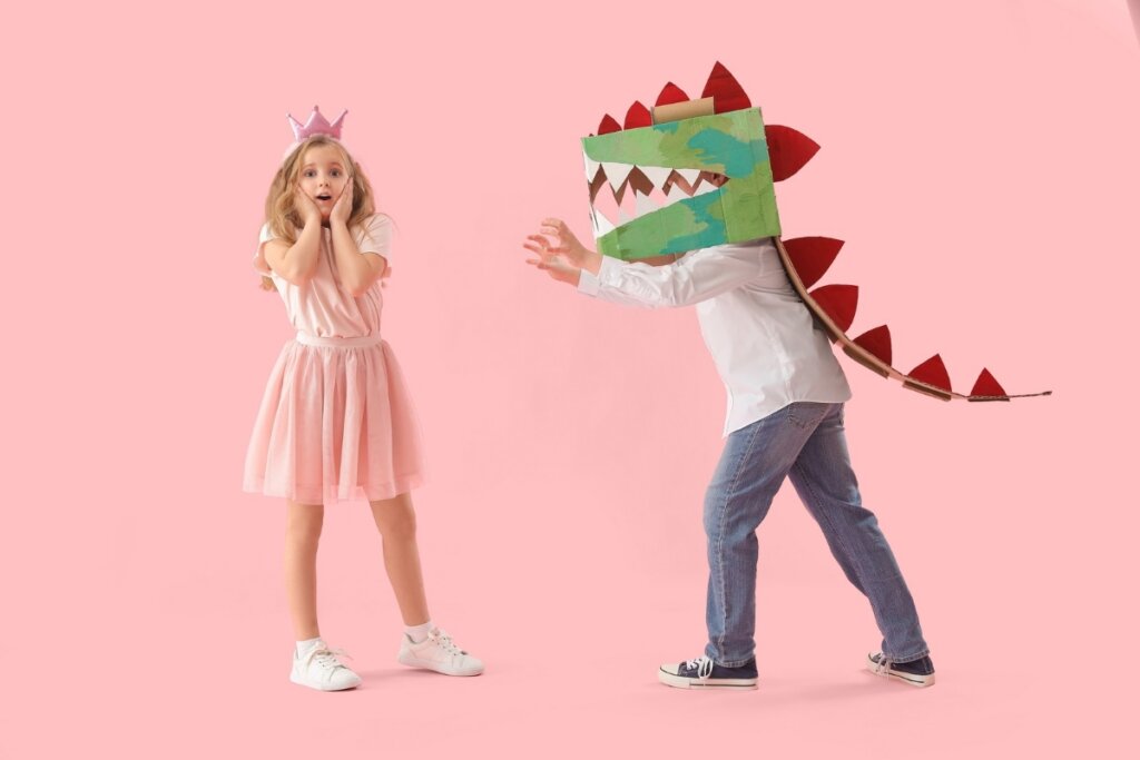 Menina vestida de princesa brincando com um menino com uma cabeça de dinossauro de papel