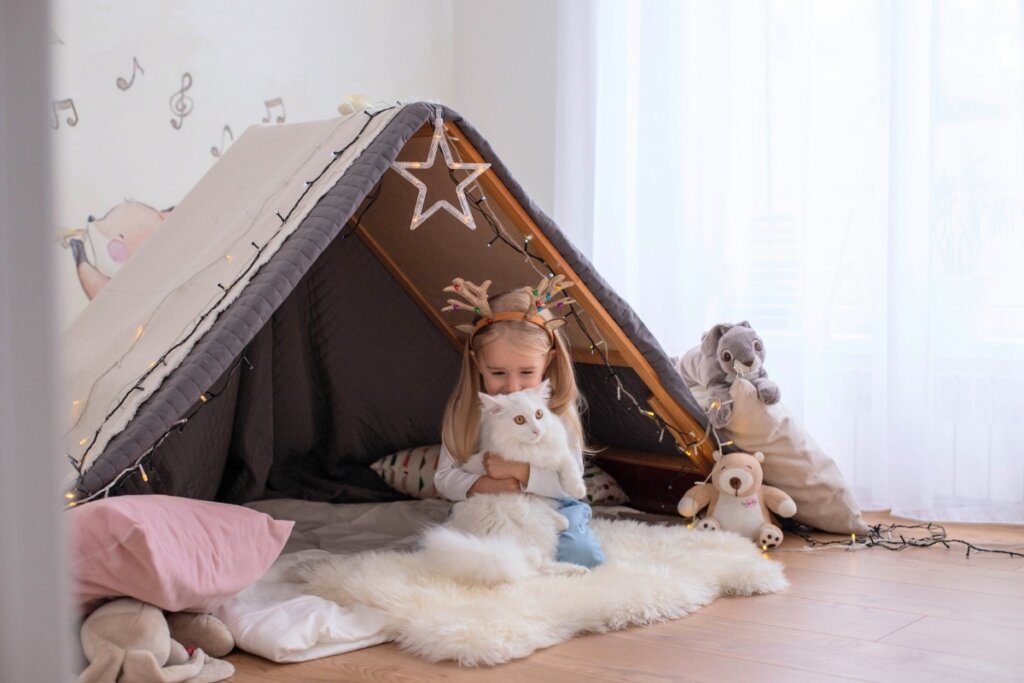 Menina dentro de uma cabana de cobertor com estrelas brincando com um gato