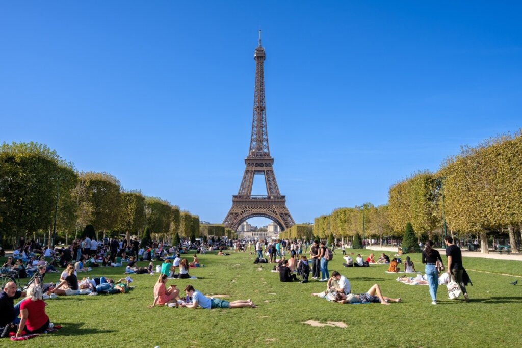 Campo de Marte com pessoas sentadas na grama com a Torre Eiffel ao fundo 