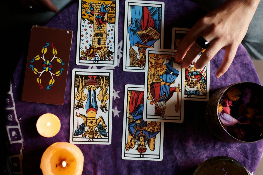 Mão feminina fazendo uma tiragem de tarot em cima de um pano roxo com vela