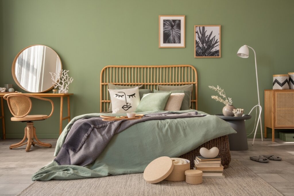 Quarto com parede verde com quadros, cama, cabeceira e mesa de cabeceira de madeira