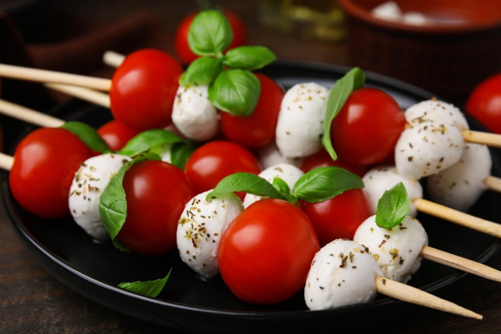 Espetinhos caprese com tomate e queijo de búfala em cima de um prato preto