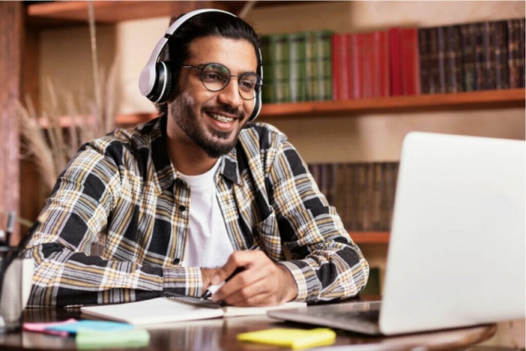 Homem sentado usando fone e mexendo em notebook