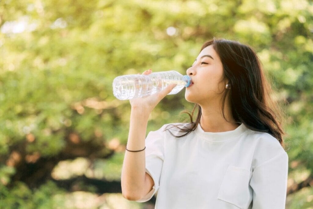Mulher em um parque bebendo água em uma garrafa descartável 