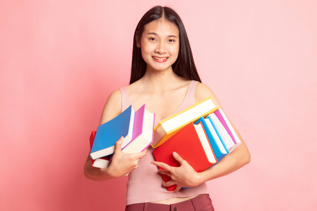 Menina sorrindo segurando livros em frente a um fundo rosa