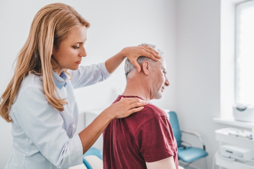 Médica em pé olhando o ombro de um homem de meia-idade sentado 