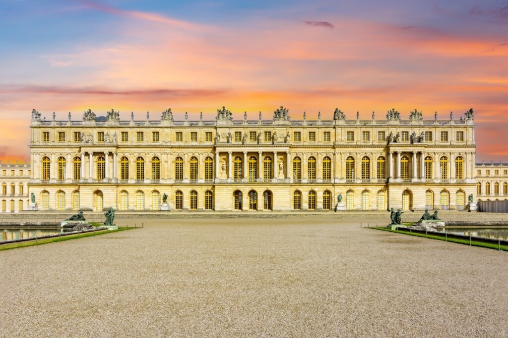Vista da arte da frente do  Palácio de Versalhes no fim da tarde com céu azul e rosa 