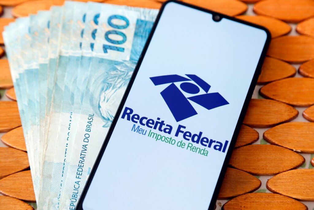 Celular logando no aplicativo da Receita Federal do lado de notas de cem reais