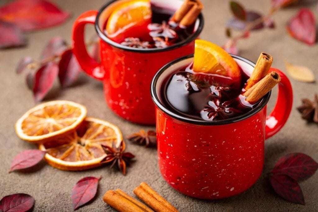 Duas canecas vermelhas com vinho quente decoradas com rodelas de laranjas