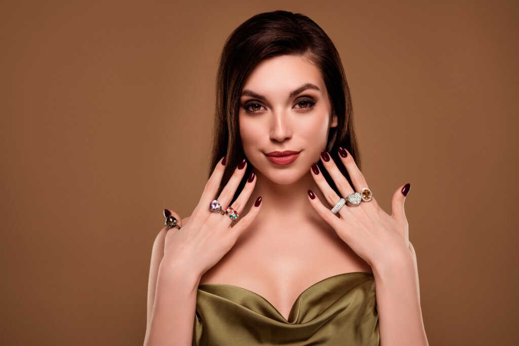 Mulher com cabelo liso, maquiada e com as unhas pintadas de preto posando para foto em um fundo marrom