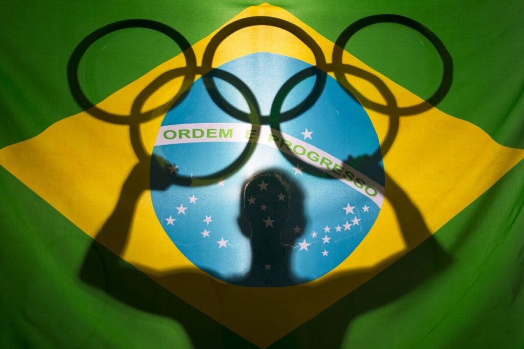 Bandeira do Brasil com sombra de homem segurando símbolo das olimpíadas