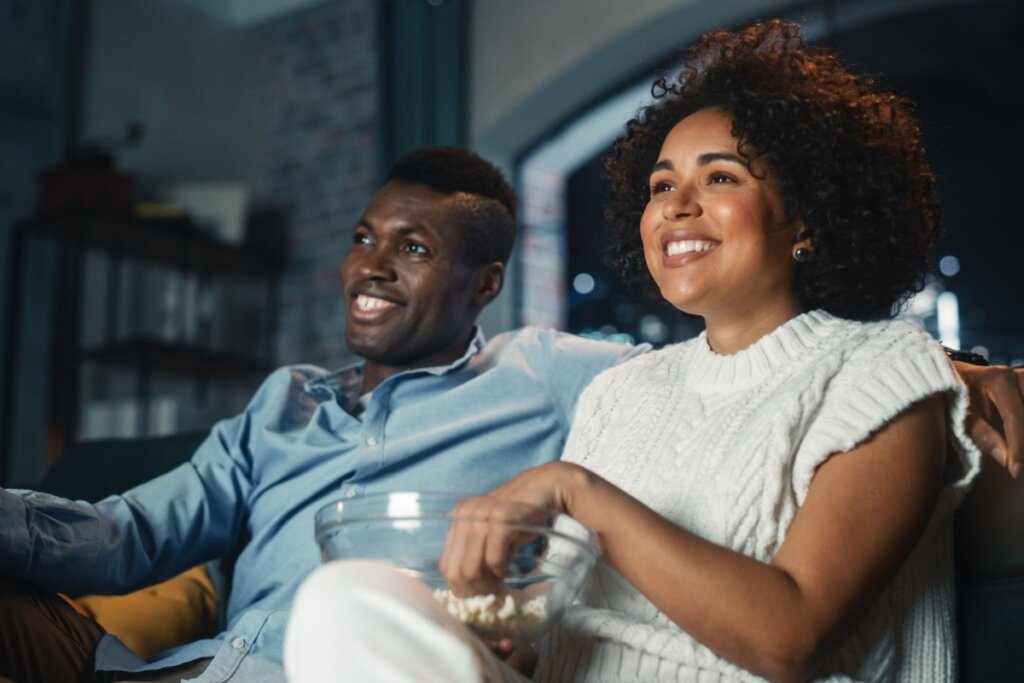 Casal sentado no sofá assistindo TV e comendo pipoca