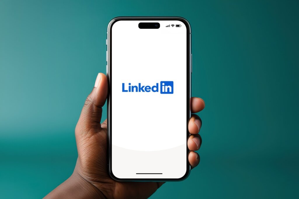 Mão segurando um celular com o símbolo do LinkedIn na tela