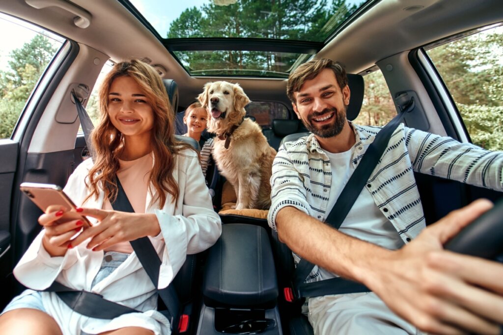 Família sorrindo em carro com cachorro no banco traseiro