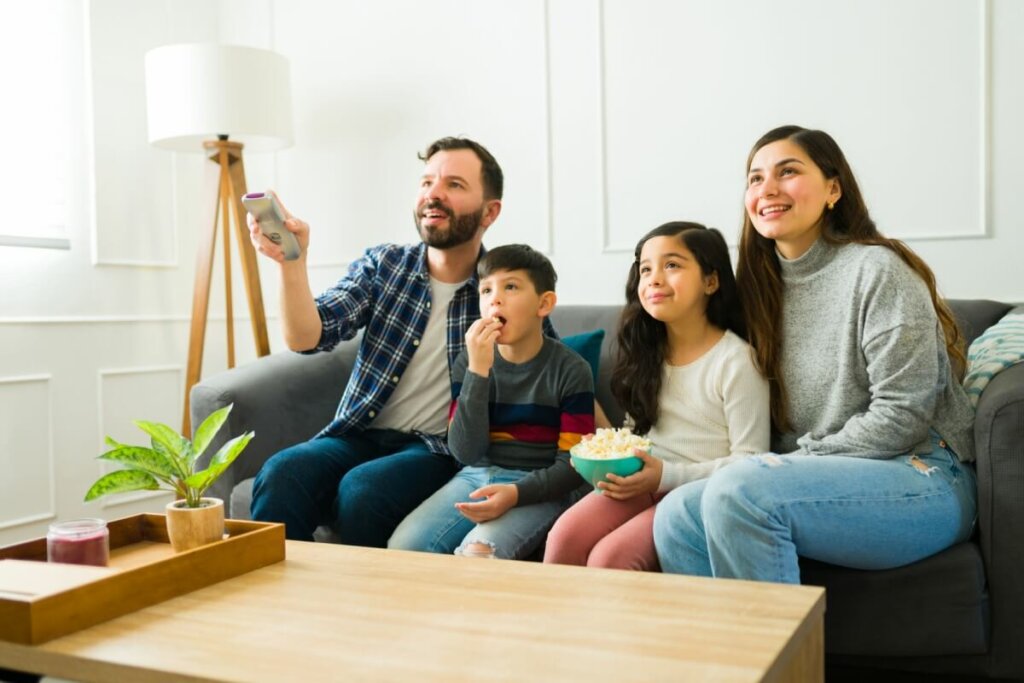 Homem, mulher e duas crianças sentadas no sofá vendo tv