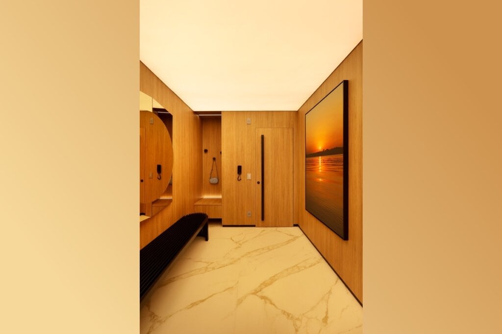 Hall de entrada com paredes e portas de madeira, piso marmorizado, iluminação suave e uma obra de arte ao fundo