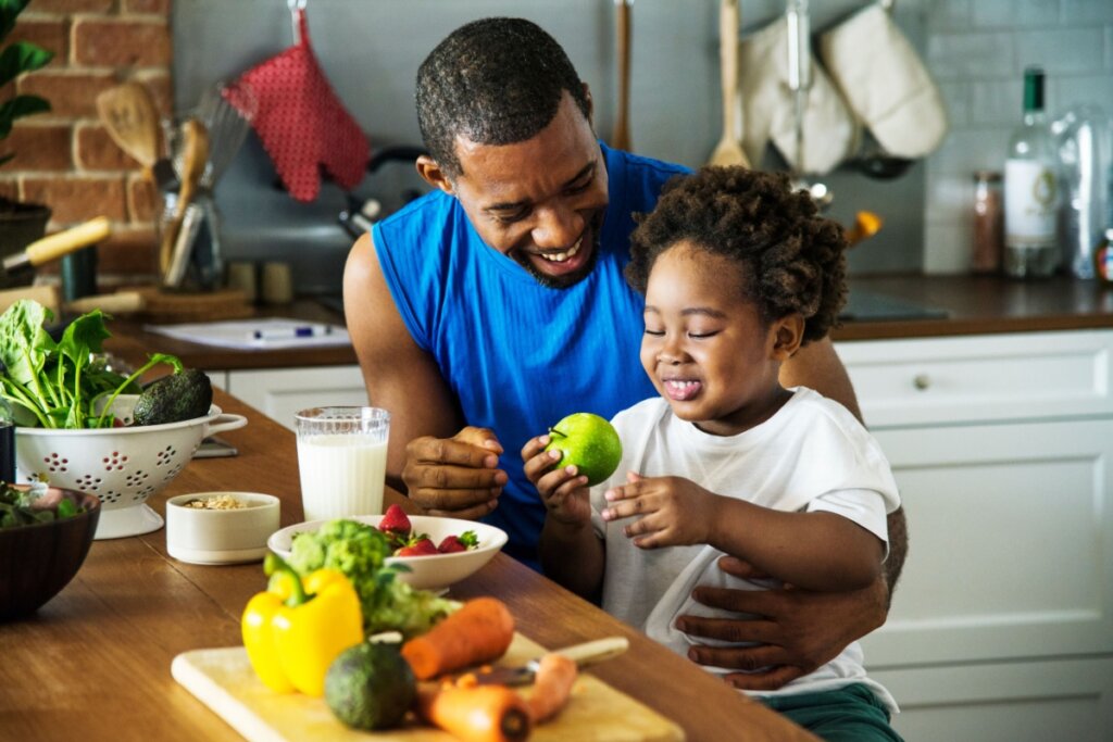 Homem e criança sorrindo comendo comida saudável em cozinha