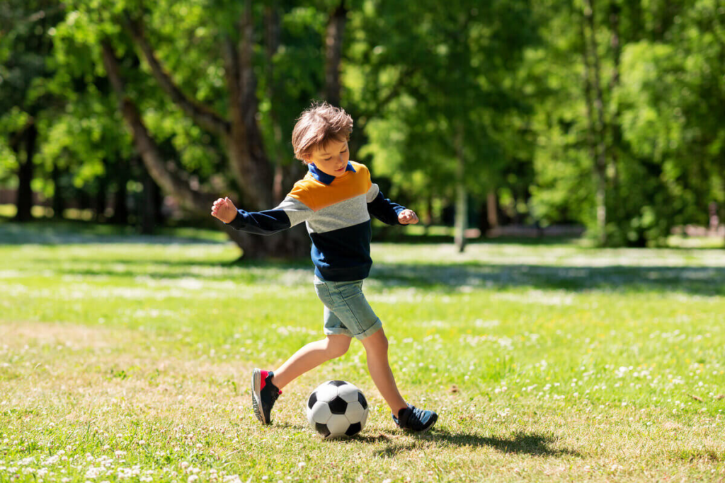 Menino jogando bola de futebol em um espaço arborizado