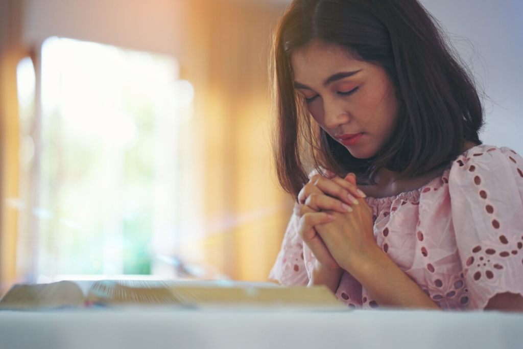 Mulher asiática ajoelhada rezando em quarto com a Bíblia