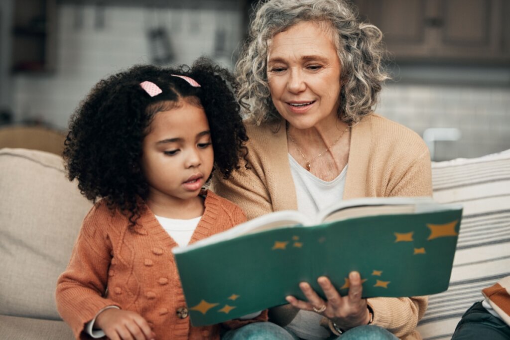 Menina e avó sentadas no sofá e lendo livro com capa verde