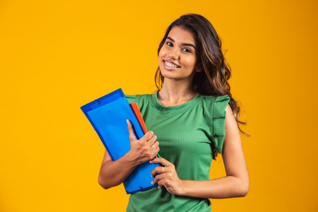 Menina estudante com livros nas mãos em um plano de fundo amarelo