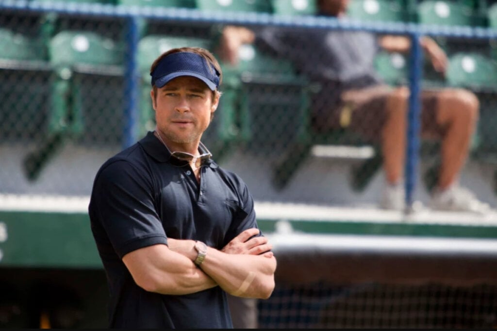 Brad Pitt de braços cruzados em "Moneyball: O Homem que Mudou o Jogo"