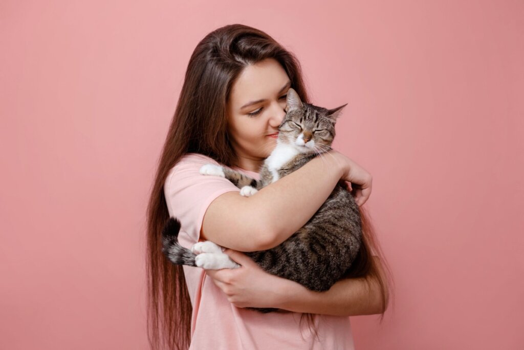 Mulher abraçando gato em um fundo rosa