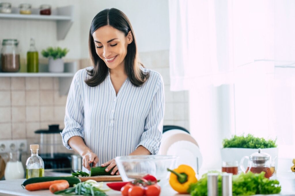 Mulher na cozinha preparando uma salada com verduras