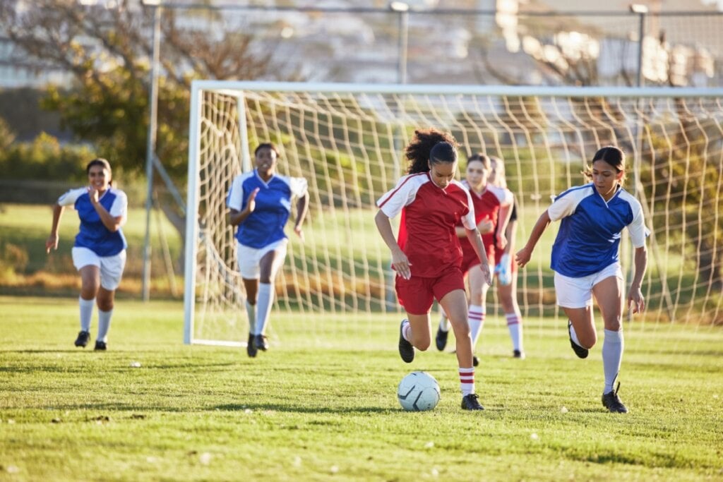 Cinco mulheres em campo jogando futebol