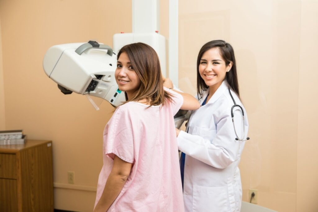 Mulher em sala de exame realizando mamografia acompanhada de uma médica